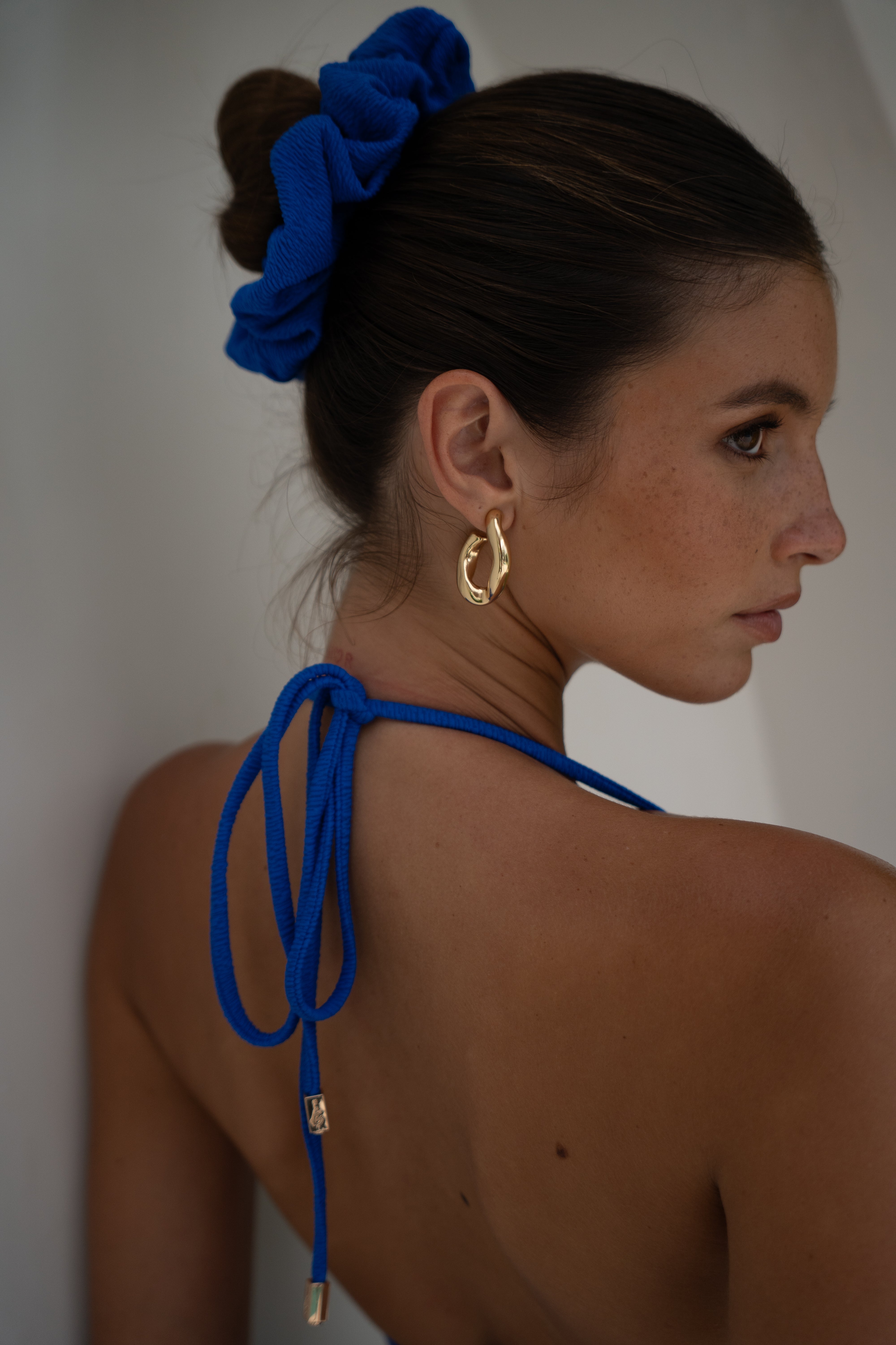 Woman with a blue scrunchie in her hair and a blue halter top against a white background