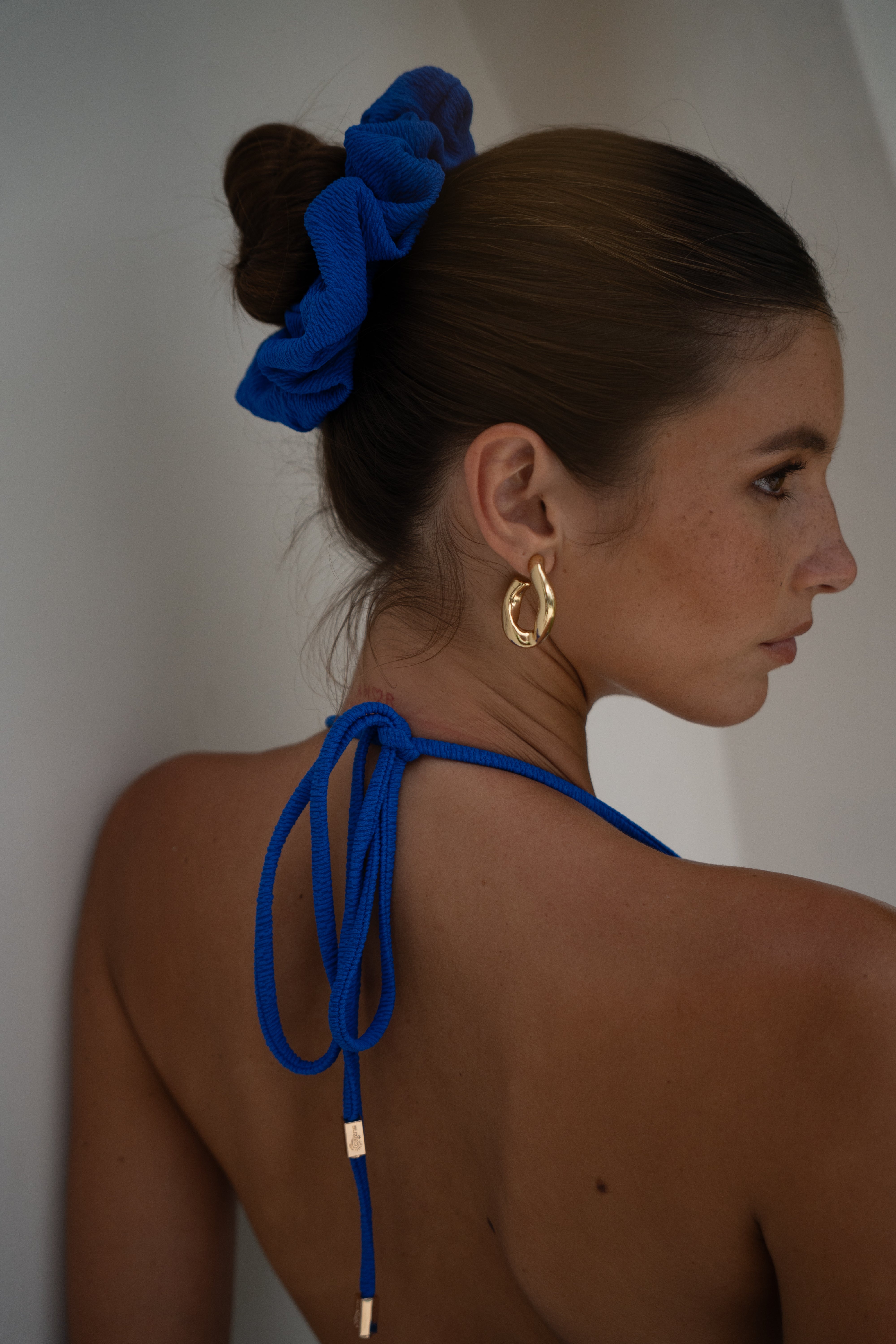Woman with a blue scrunchie and rope in her hair, wearing gold hoop earrings.