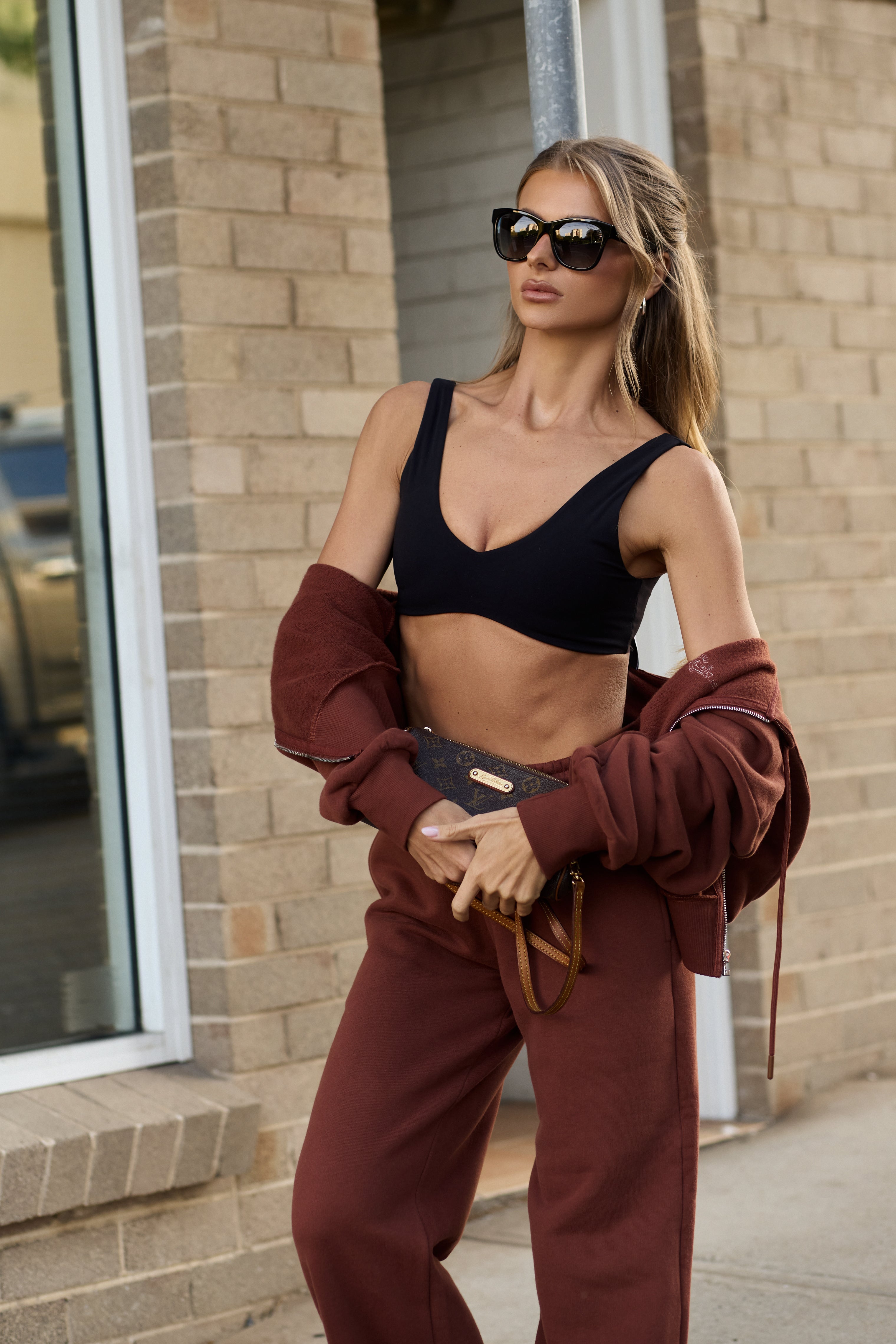 Woman in black sports bra and brown sweatpants standing outside a building.